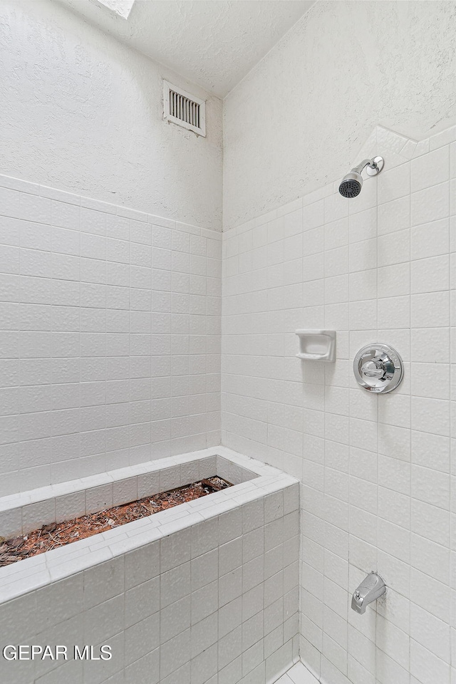 full bath featuring a textured wall, visible vents, a textured ceiling, and a tile shower