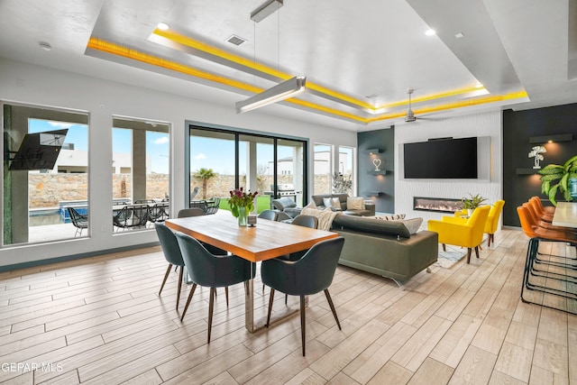 dining space with wood finish floors, visible vents, a fireplace, and a tray ceiling