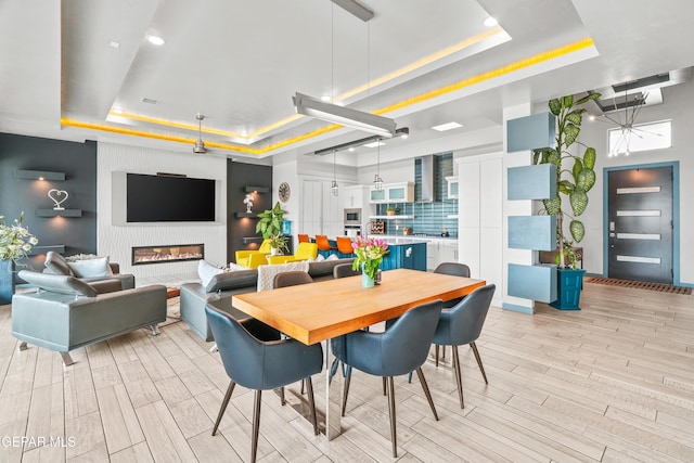 dining room with wood finish floors, a large fireplace, and a tray ceiling