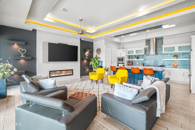 living area with a raised ceiling, a fireplace, visible vents, and light wood finished floors