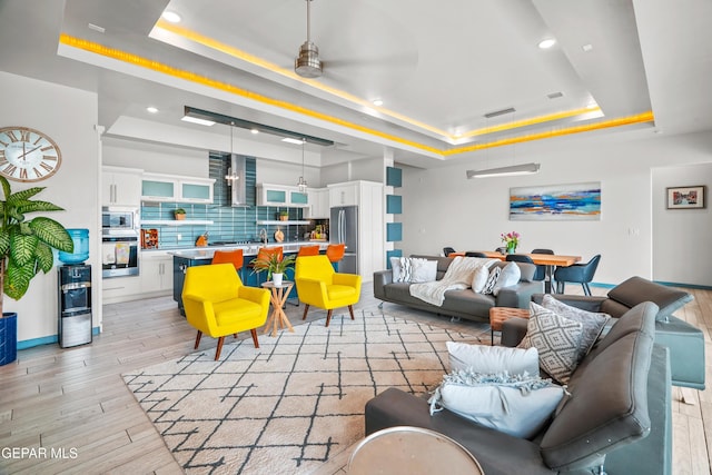 living room with light wood finished floors, visible vents, a ceiling fan, and a tray ceiling