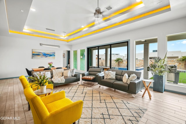 living area featuring a tray ceiling, wood finished floors, visible vents, and ceiling fan