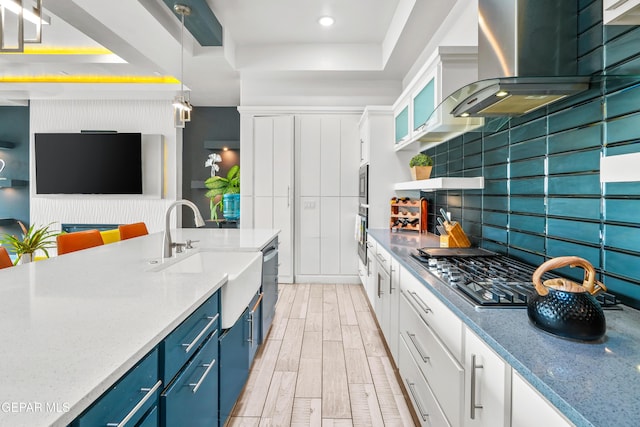 kitchen with tasteful backsplash, blue cabinets, wood tiled floor, white cabinets, and wall chimney exhaust hood