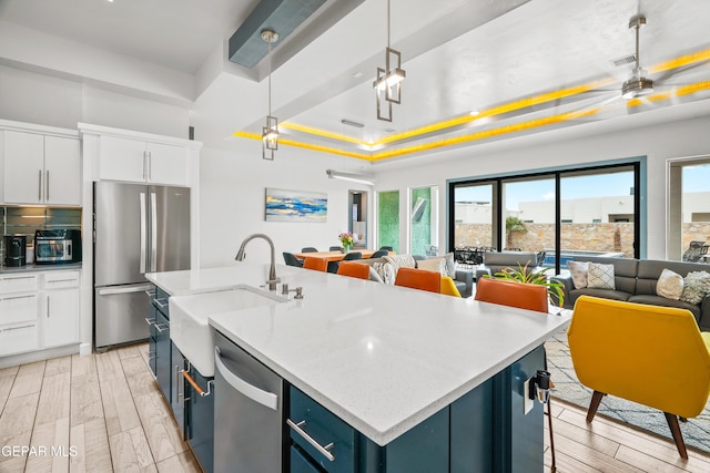 kitchen with a tray ceiling, open floor plan, appliances with stainless steel finishes, and a sink