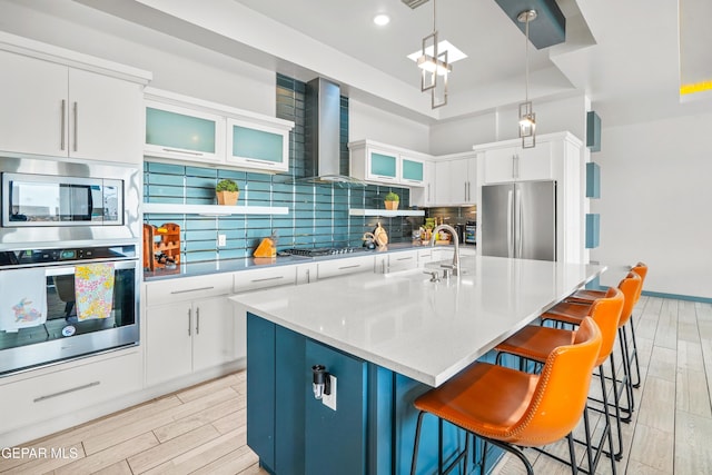 kitchen with tasteful backsplash, wood tiled floor, a breakfast bar area, stainless steel appliances, and wall chimney exhaust hood