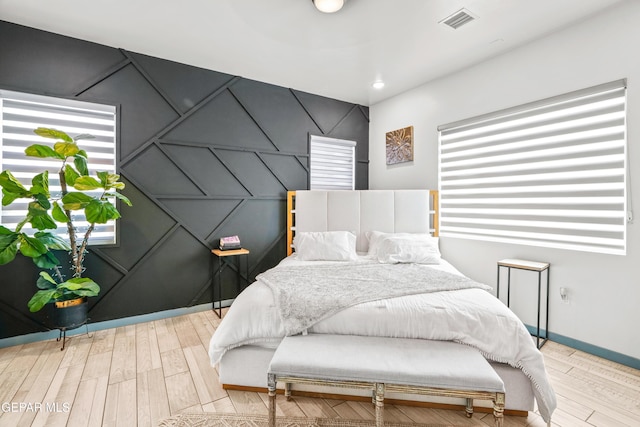 bedroom featuring an accent wall, baseboards, visible vents, and light wood finished floors