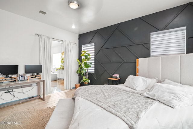 bedroom with an accent wall, a decorative wall, wood finished floors, and visible vents