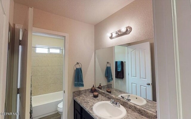 full bath with a textured ceiling, toilet, vanity, and shower / bathing tub combination