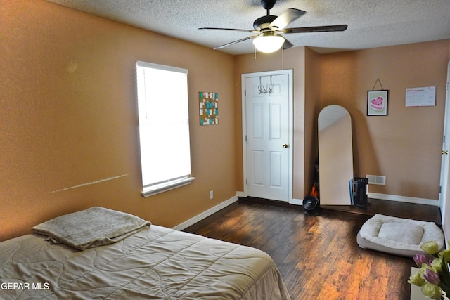 bedroom featuring wood finished floors, visible vents, baseboards, ceiling fan, and a textured ceiling