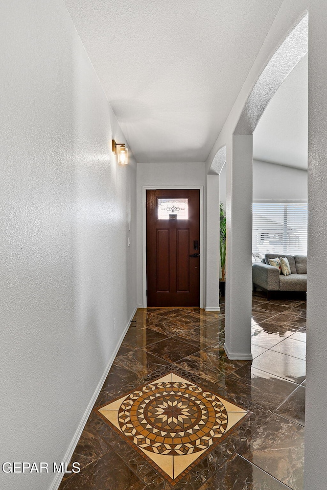 foyer featuring baseboards, a textured ceiling, marble finish floor, and a textured wall