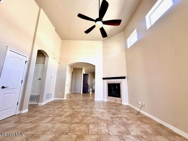 unfurnished living room with visible vents, a ceiling fan, arched walkways, a fireplace, and baseboards