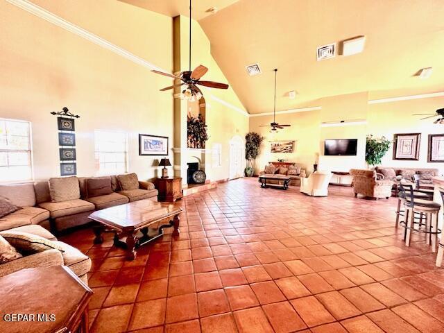 living area featuring tile patterned flooring, visible vents, a towering ceiling, and ceiling fan