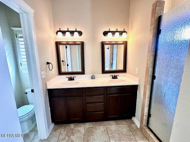 bathroom with double vanity, tile patterned floors, toilet, and a sink