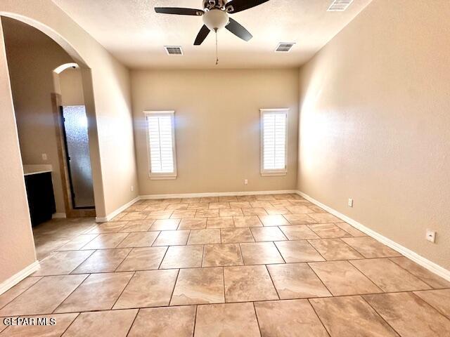 empty room with baseboards, arched walkways, visible vents, and ceiling fan