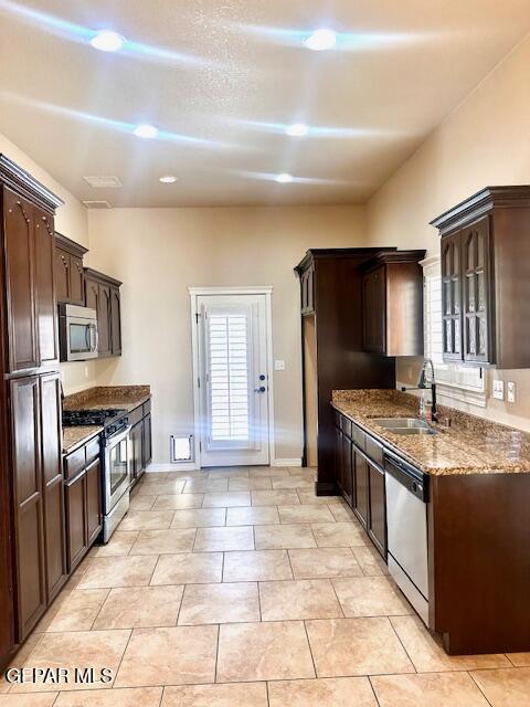 kitchen with dark stone countertops, dark brown cabinets, appliances with stainless steel finishes, and a sink