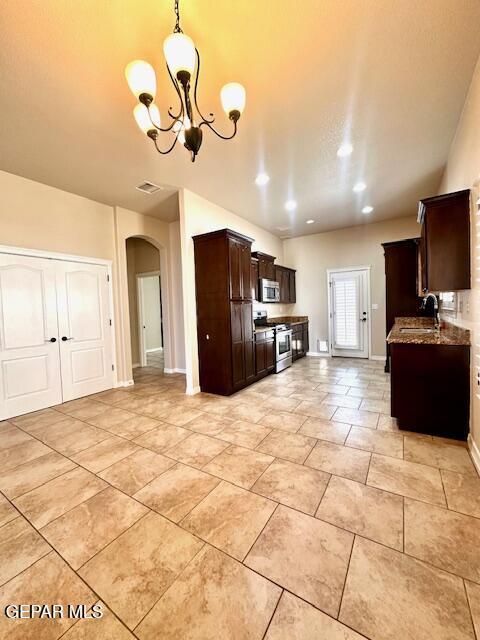 kitchen with arched walkways, a sink, stainless steel appliances, dark brown cabinetry, and a notable chandelier