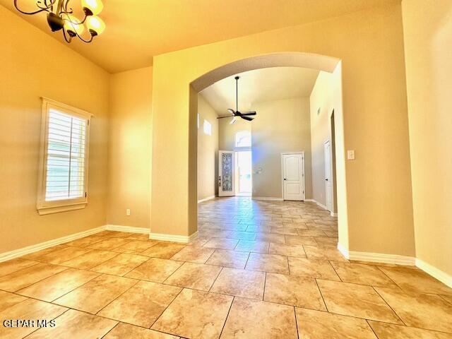 unfurnished room featuring arched walkways, light tile patterned floors, ceiling fan with notable chandelier, and baseboards