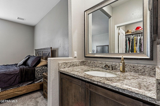 bathroom with visible vents, vanity, a walk in closet, and a textured wall