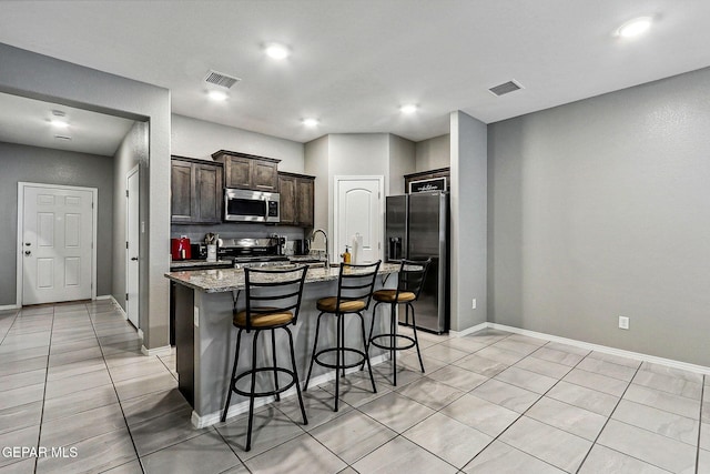 kitchen featuring visible vents, a breakfast bar, stainless steel microwave, refrigerator with ice dispenser, and range