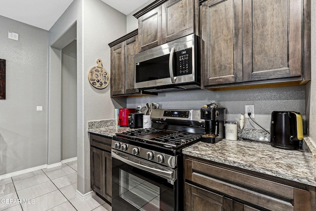 kitchen with light tile patterned floors, light stone countertops, baseboards, dark brown cabinets, and appliances with stainless steel finishes