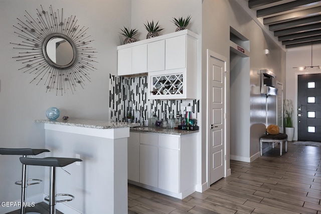 bar featuring decorative backsplash, beamed ceiling, wood finished floors, and indoor wet bar