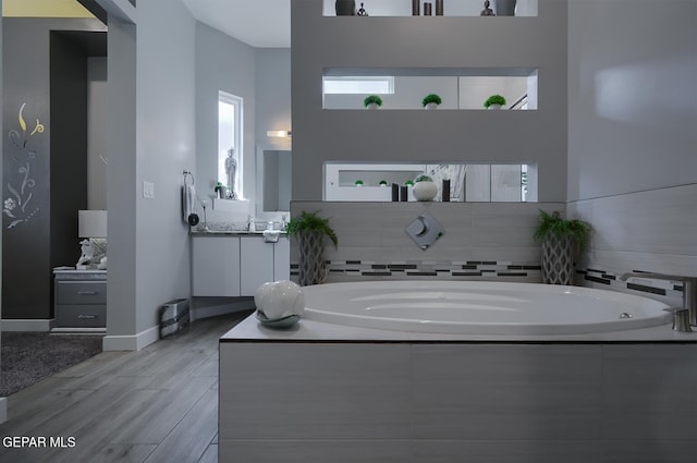 bathroom with vanity, a bath, wood finished floors, and baseboards