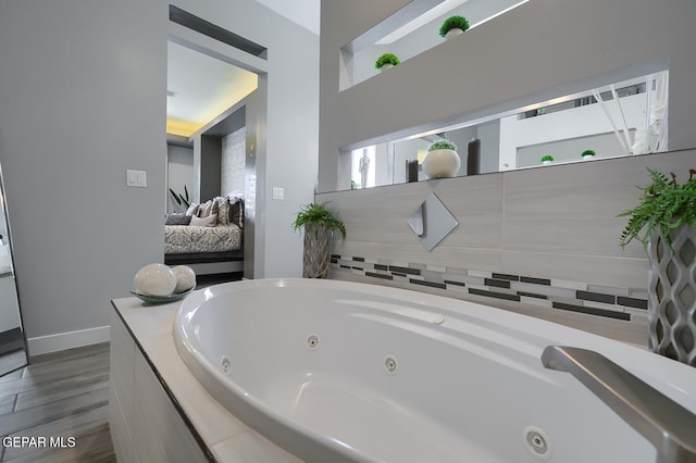 ensuite bathroom with a tub with jets, ensuite bath, baseboards, and wood finished floors