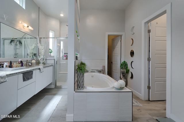 bathroom with wood finished floors, a shower stall, baseboards, a bath, and vanity