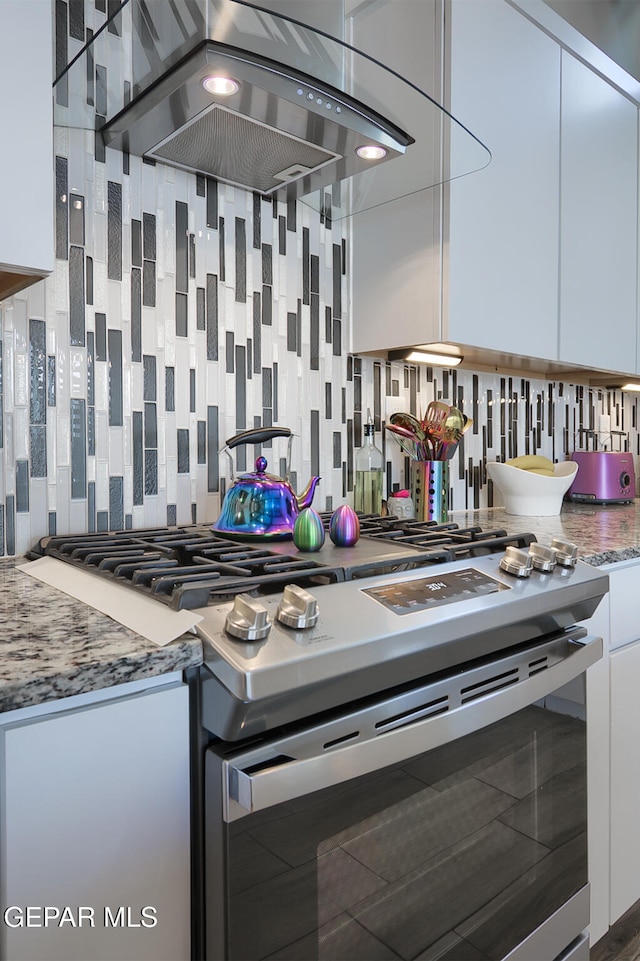 kitchen featuring stainless steel gas range oven, backsplash, extractor fan, and white cabinets