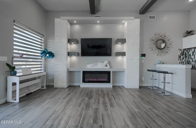 unfurnished living room with beamed ceiling, visible vents, and wood finished floors