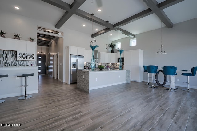 kitchen with a center island with sink, a towering ceiling, beamed ceiling, stainless steel fridge, and backsplash