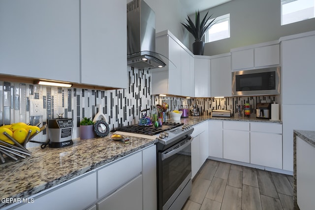 kitchen with stainless steel microwave, gas range, backsplash, and wall chimney range hood