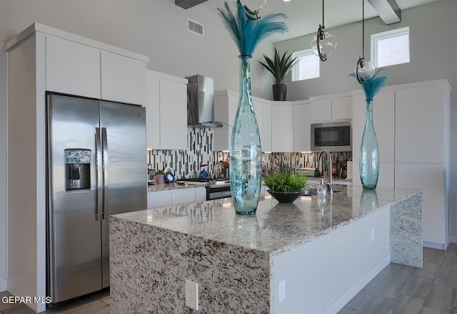 kitchen featuring visible vents, a sink, stainless steel appliances, a towering ceiling, and wall chimney exhaust hood