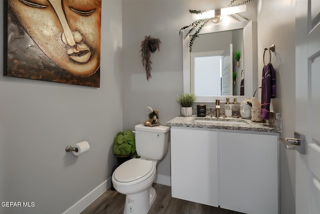 half bathroom with baseboards, toilet, wood finished floors, and vanity