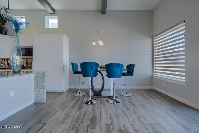 dining space with light wood finished floors, beamed ceiling, and baseboards