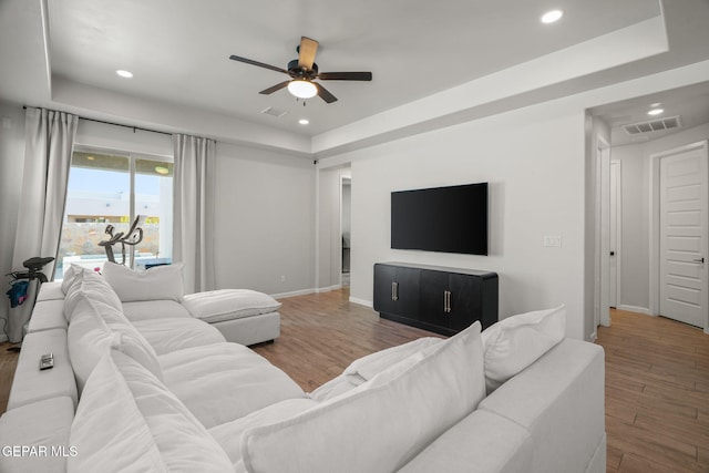 living room featuring a raised ceiling, recessed lighting, wood finished floors, and baseboards