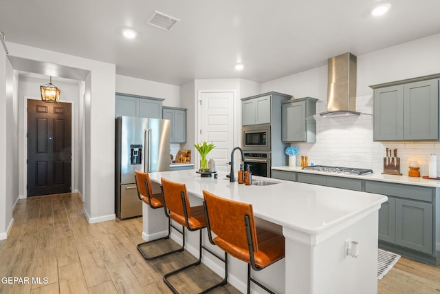 kitchen with visible vents, wall chimney range hood, light wood-type flooring, appliances with stainless steel finishes, and a sink