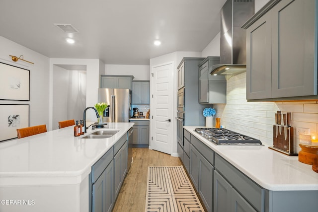 kitchen featuring gray cabinets, stainless steel appliances, wall chimney range hood, and a sink