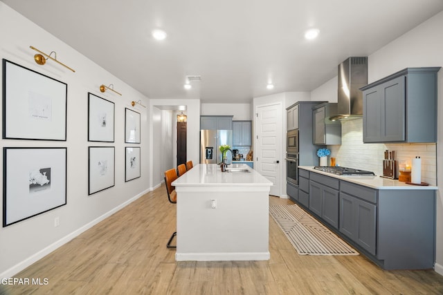 kitchen featuring wall chimney range hood, light countertops, decorative backsplash, appliances with stainless steel finishes, and a sink