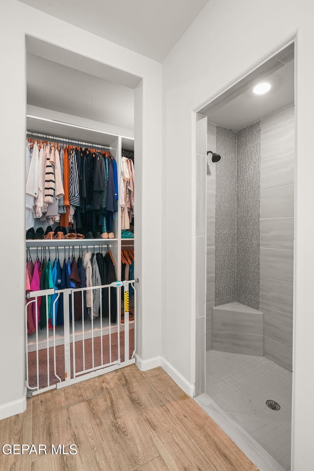 full bath featuring a walk in closet, wood finished floors, baseboards, and tiled shower