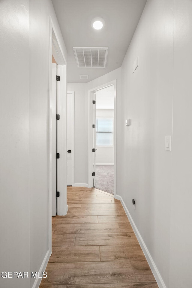 hall featuring visible vents, baseboards, and wood finished floors