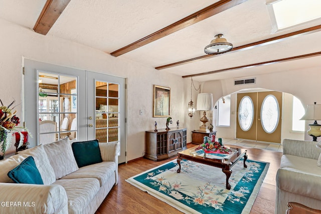 living room featuring wood finished floors, visible vents, beam ceiling, arched walkways, and french doors