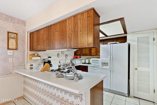 kitchen with light tile patterned floors, white appliances, a peninsula, and light countertops