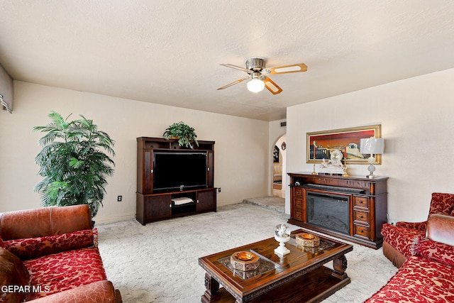 living room featuring carpet flooring, arched walkways, a glass covered fireplace, a textured ceiling, and a ceiling fan