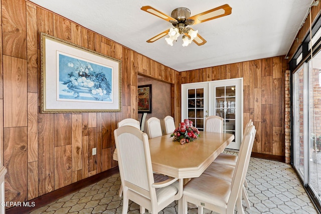 dining area with a ceiling fan, french doors, wooden walls, baseboards, and light floors