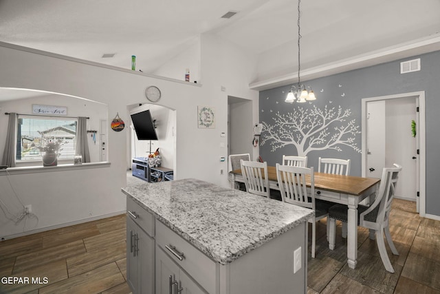 kitchen with visible vents, wood tiled floor, a center island, and vaulted ceiling