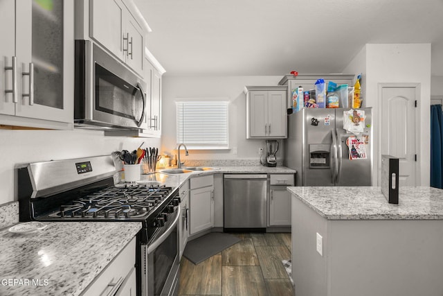 kitchen with dark wood-type flooring, gray cabinetry, a sink, light stone counters, and stainless steel appliances