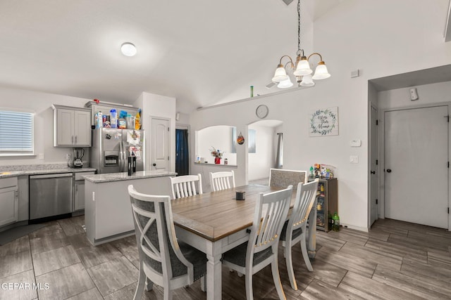 dining space with arched walkways, wood finish floors, an inviting chandelier, and lofted ceiling