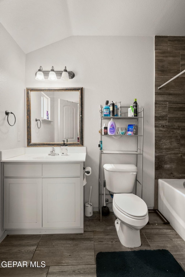 full bathroom with toilet, wood finished floors, lofted ceiling, bathing tub / shower combination, and vanity