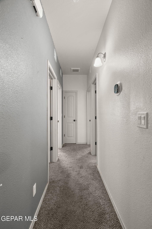 hall with a textured wall, visible vents, carpet floors, and baseboards